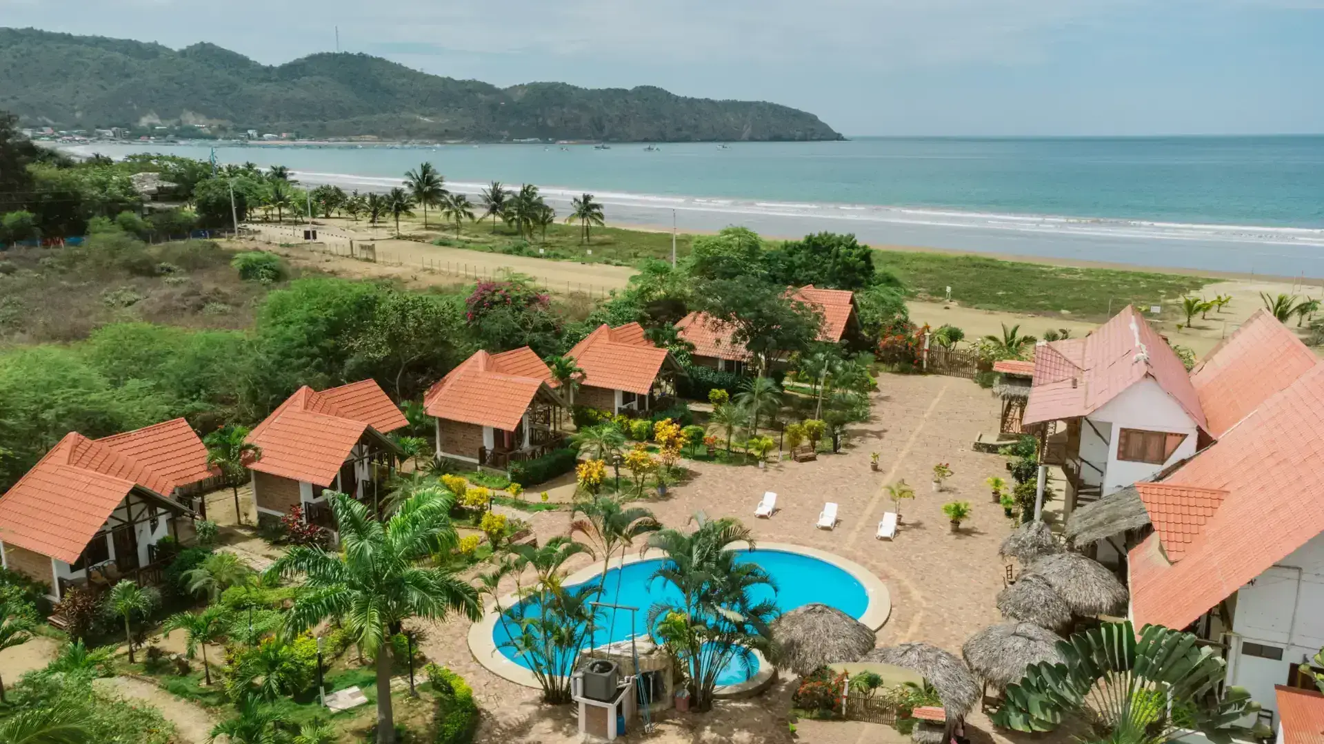 Vista aérea de Hostería Oceanic — cabañas con techos de teja, piscina azul y jardines tropicales frente al Pacífico en Puerto López, Manabí, Ecuador